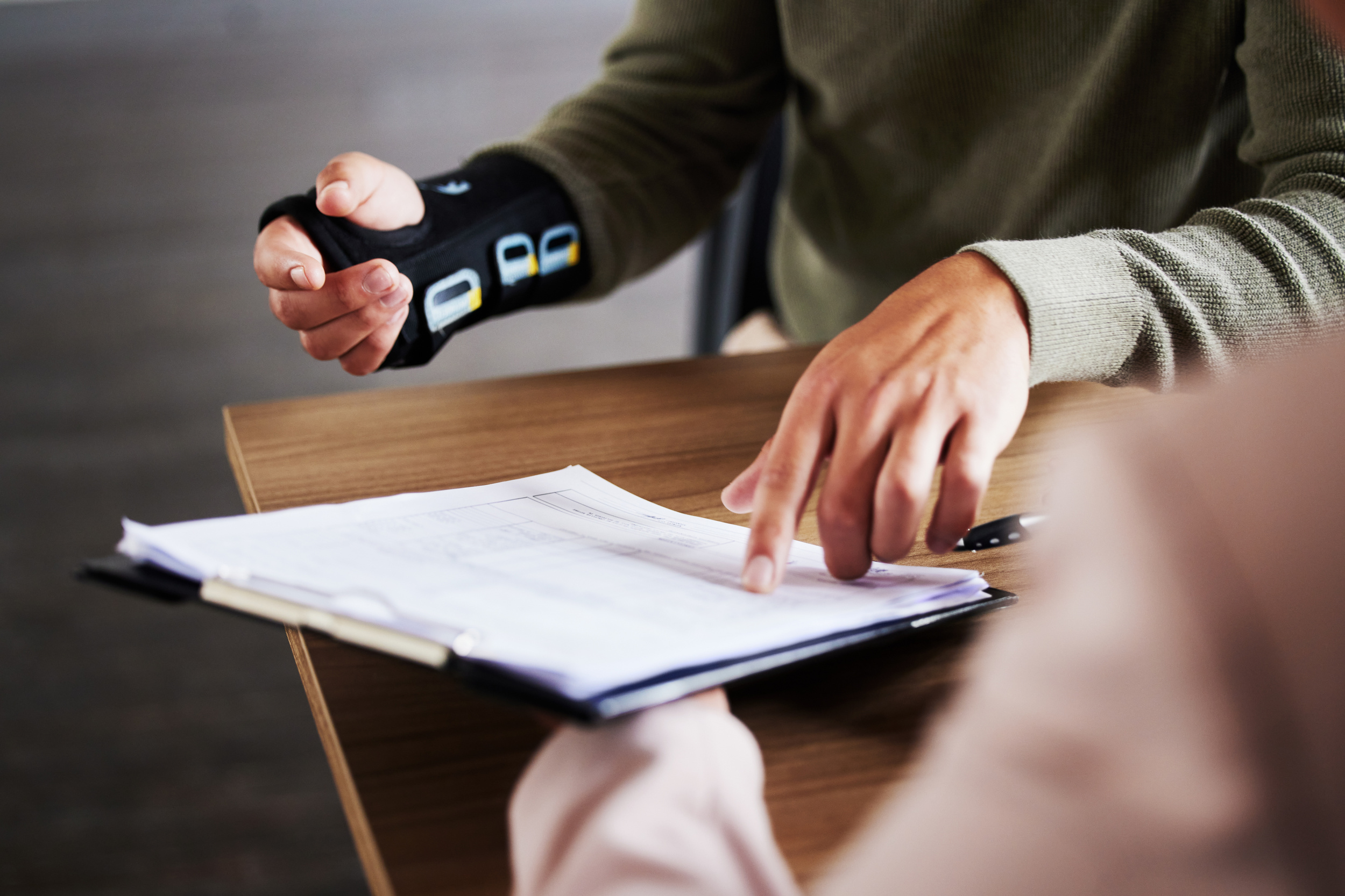 Injury, compensation and man hands with insurance documents, legal contract and paperwork. Disability, accident and people in lawyer or attorney meeting for advice, agreement or policy report closeup.